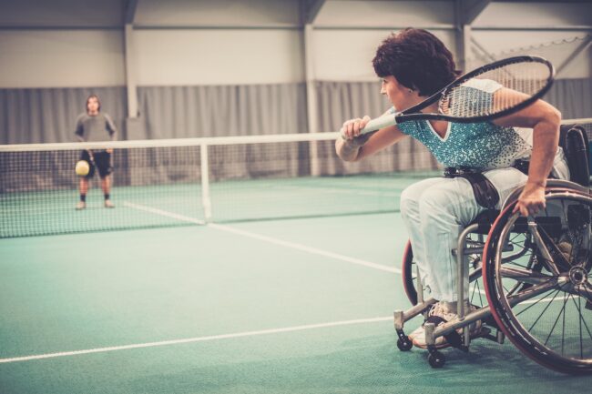 Disabled mature woman on wheelchair playing tennis on tennis court