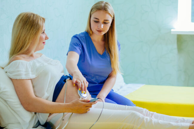 Blond young midwife examination belly of pretty blond pregnant woman with CTG scanning in practice. Pregnancy care. cardiotocography fetal heartbeat examination.